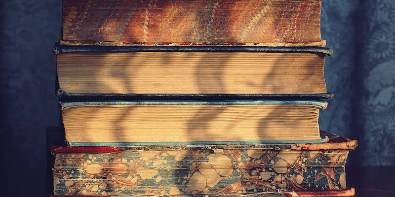 A stack of old vintage books on a wooden table with decorative marbled covers.